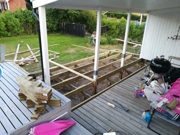 Pågående ombyggnation av en altan med träreglar och verktyg under ett takområde.