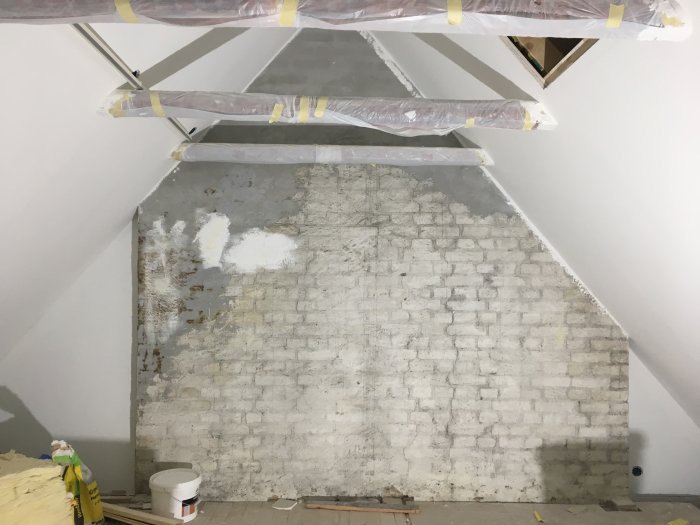 Renoveringsprojekt av en ojämn tegelvägg med missfärgningar och vitmålade fläckar under renovering.