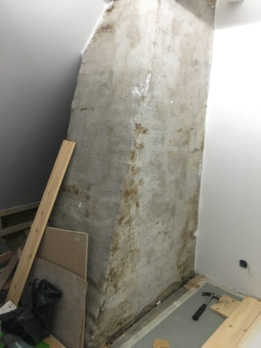 Större bild av en murstock med missfärgningar och rester av vit färg i ett rum under renovering.