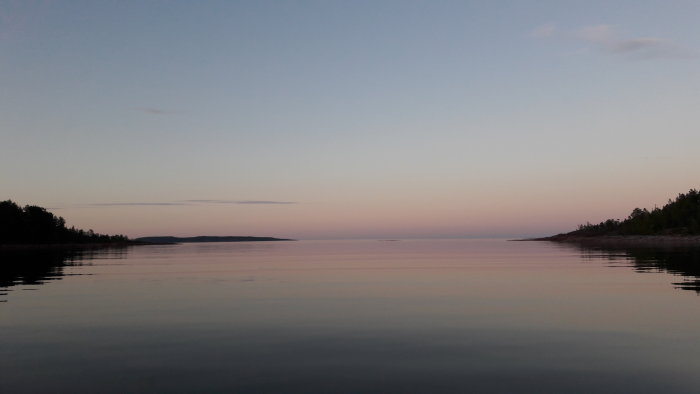 Spegelblank sjö vid skymning med pastellfärgad himmel och trädbevuxna kuster.