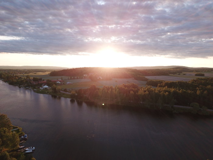 Solnedgång över landskap med flod, fält, skogar och byggnader. Dronevy.