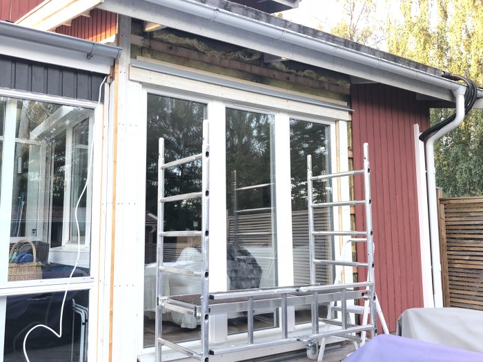 Delvis avlägsnad träpanel på hus med fönster och stegar, renoveringsprojekt på började.