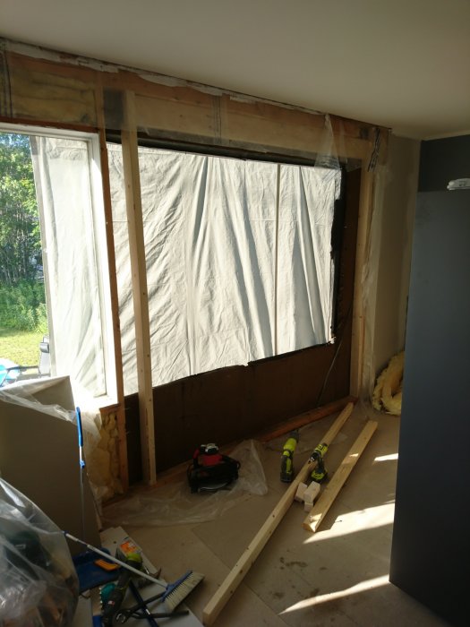 Renoveringsprojekt där en gammal fönsteröppning är täckt med presenning, verktyg och material på golvet.