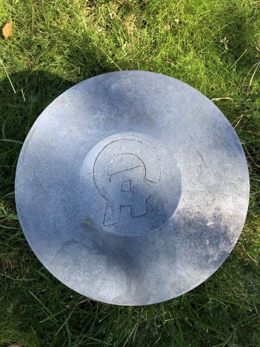 Metalllock på gräs med ingraverad symbol visande bokstäverna 'CA' eller 'GA' som identifieringshjälp för en brunnpump.