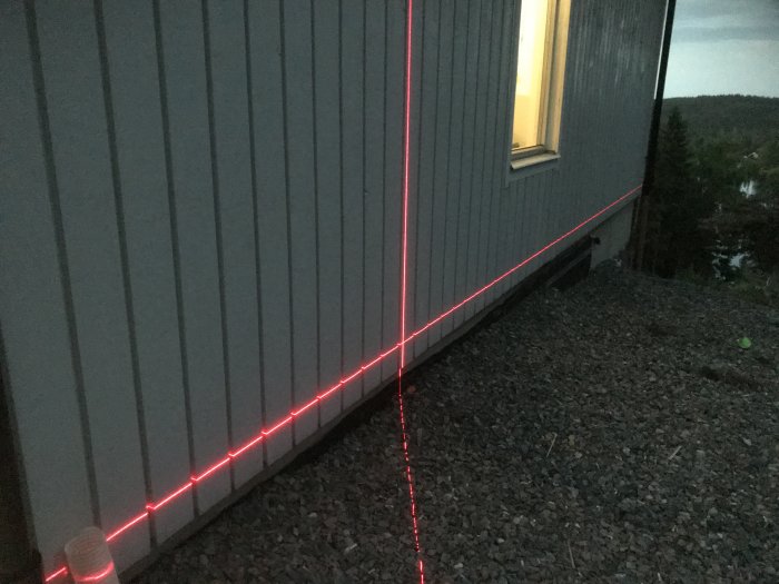 Laserstråle markerar altanens inre bärlinje mot husvägg under skymning.