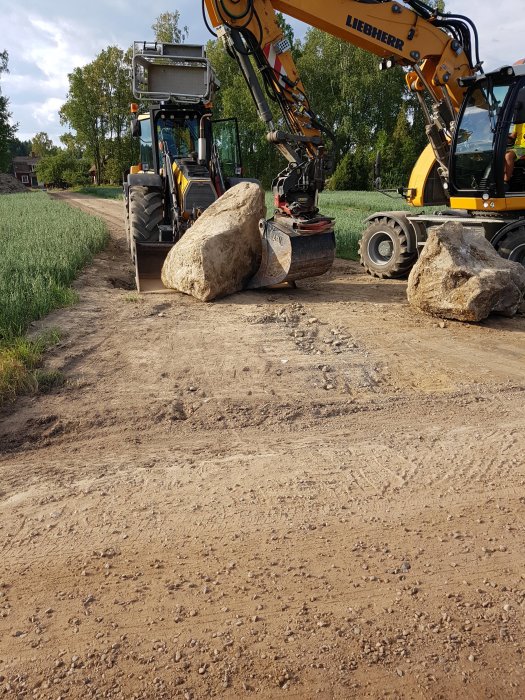 Grävmaskin som har tagit bort stora stenar från en jordväg, redo för grusläggning.