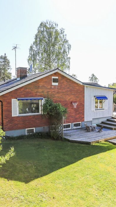 Rött tegelhus med ljusblå träpanelutbyggnad, grön gräsmatta och trädäck.