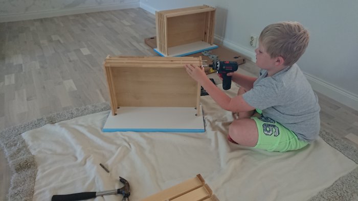 Barn monterar trädelar till en låda med skruvdragare på golvet.