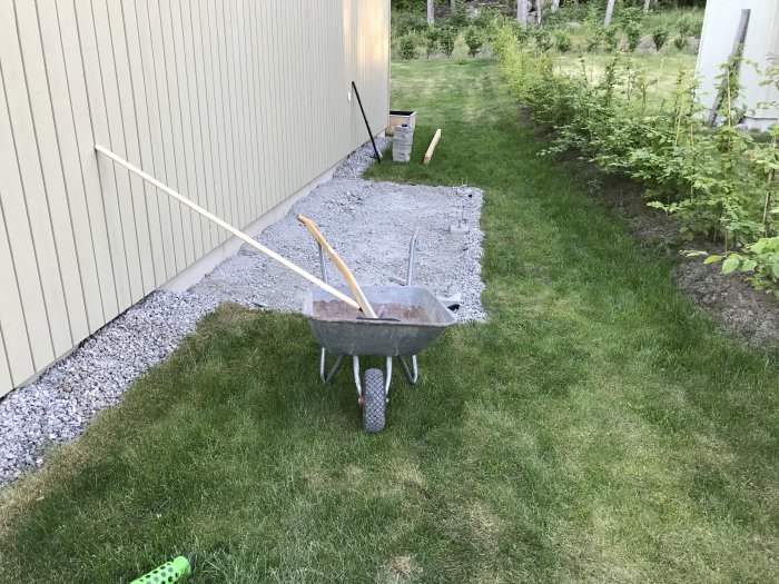 Preparations for building an outdoor storage with a wheelbarrow, dug holes, and a layer of gravel.