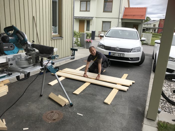 Person som mäter panelbrädor nära en kap- och gersåg utanför ett hus.