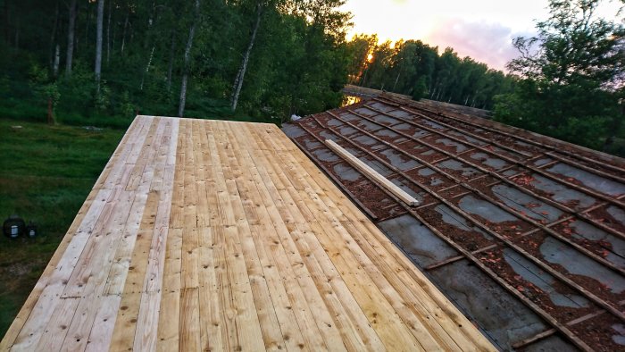 Färdiglagt trägolv på en veranda med otillverkad del av taket synlig, omgiven av natur.