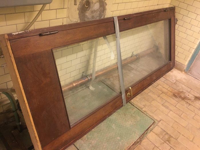 En delvis öppen dubbeldörr med träram och stora glasrutor mot en källarlokal med rör i bakgrunden.