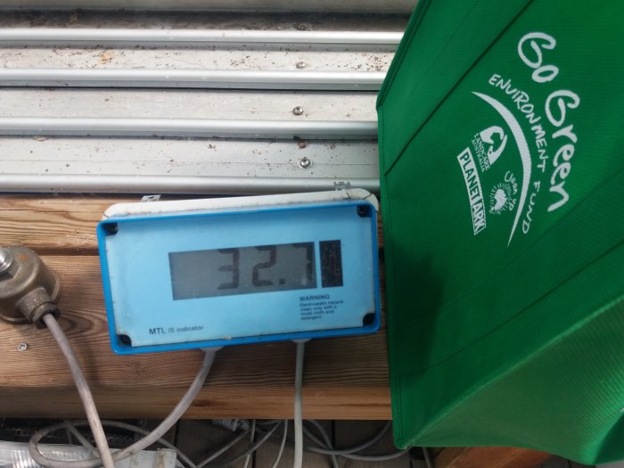 Termometer visar 32.1 grader nära ett pooltak och en grön väska märkt "GoGreen".