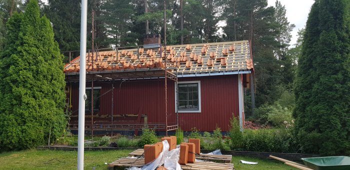 Röd trävilla med påbörjat takarbete, takpannor upplagda och byggnadsställning runt huset.