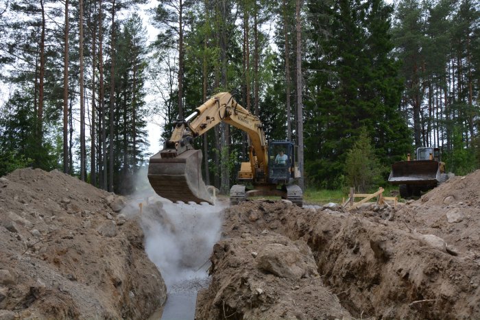 Grävmaskin arbetar med att gräva ut rännor för plintgjutning på en skogstomt.