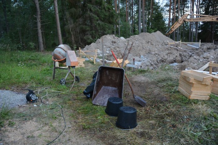 Byggplats med grävmaskin, gjutformar och material för gjutning av plintar och socklar.