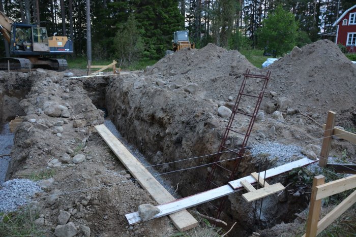 Gjutningsarbete av socklar och plintar i en grävd grund med armeringsjärn som sticker upp, vid en byggplats i skymningen.