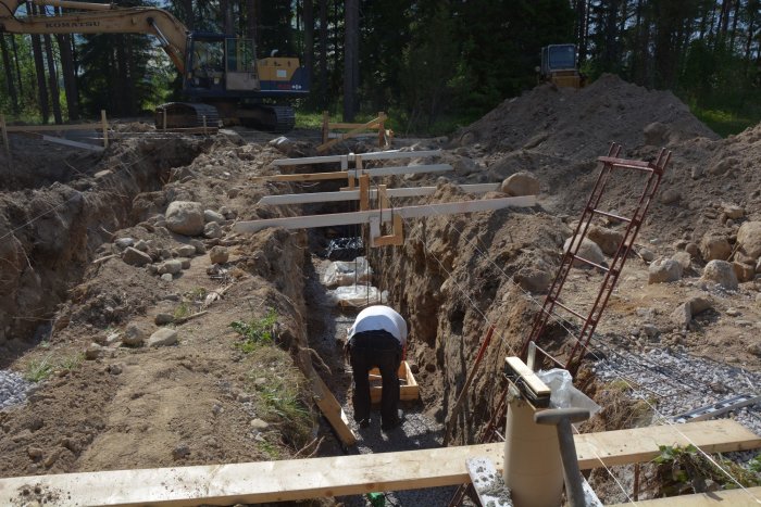 Byggarbetsplats där grunden för ett hus förbereds med en person som arbetar vid gjutna betongsocklar och armeringsjärn.