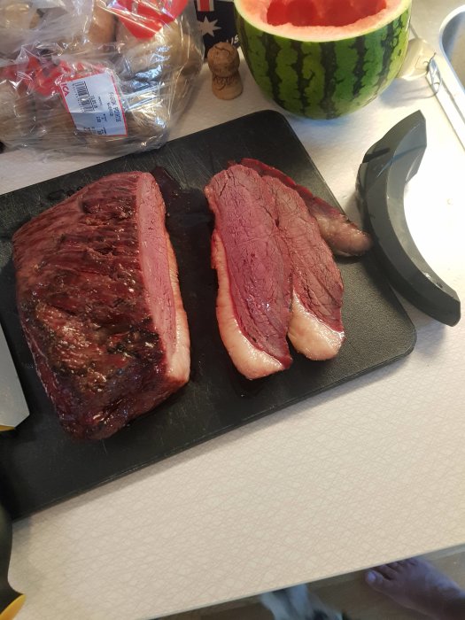 Skivad picanha på skärbräda med vattenmelon och kryddor i bakgrunden.