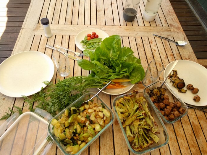 Lunchmåltid på träbord med hemodlad stekt potatis, squash, ugnsbakad blomkål, morötter, tomater, ärtor, sallad och vegetariska bullar.