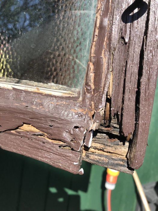 Närbild av ett gammalt fönster med upprutten träkant och sprucket kitt.