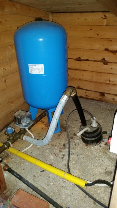 Vattenpump och trycktank i ett pumphus med synliga rör och ledningar.
