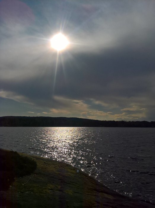 Kvällssol över sjö med reflekterande vattenskimmer och mörka moln på himlen.