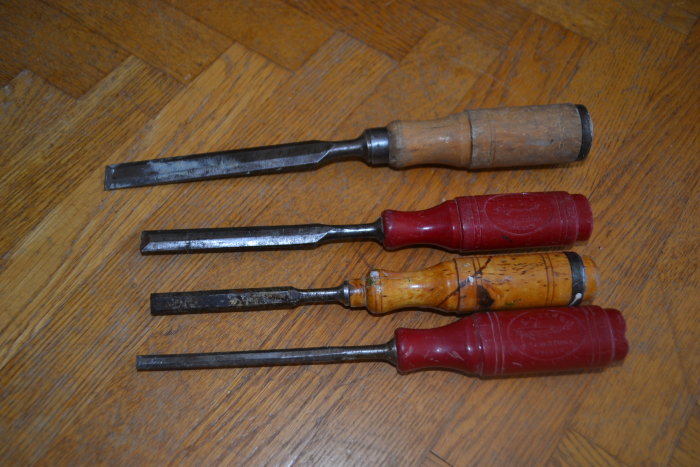 Fyra stämjärn med handtag i trä och plast, upplagda på ett trägolv. Olika storlekar med synliga bruksspår.