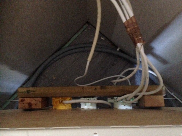 Elektrisk installation bakom köksskåp med synliga kablar och dosor skruvade på en träregel.