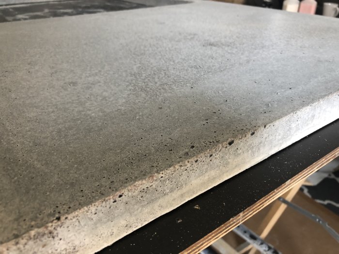 Betonbänkskiva med vitflammiga inslag och flera hål, ligger på en trähylla.