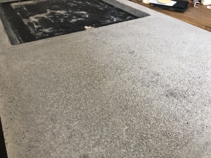 Vänd betongplatta med vitflammiga mönster och många små hål synliga vid närbild, utan armering.