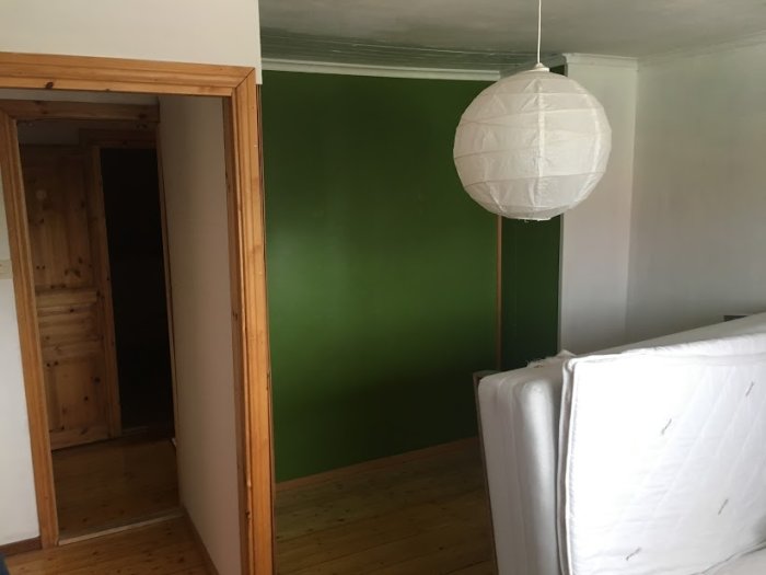 Ett rum före renovering med olivgröna väggar, oskyddad vit soffa och papperslampa.