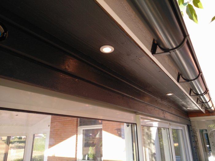 Spottar installerade i ett svartmålat takfot ovanför fönster, med synlig ledning och rör.