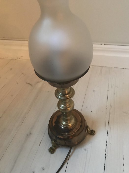En loppisfyndad mässingslampa på ett trägolv, utan synlig sladd eller stickpropp.