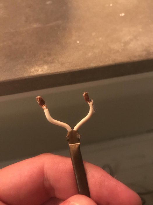 Hand som håller en elektrisk sladd med avskalade och uppdelade koppartrådar vid änden.
