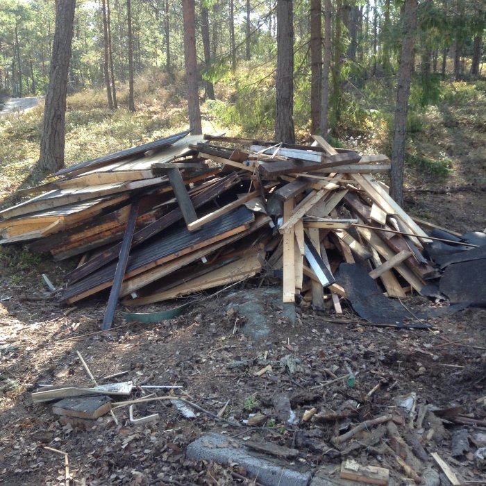 En hög med gamla demonterade träplankor och byggavfall i en skogsmiljö.