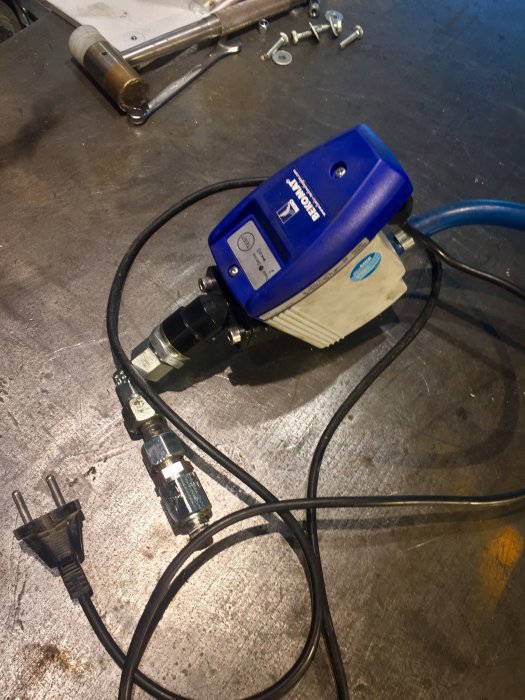Automatisk dräneringsventil för kompressor på verkstadsbänk med verktyg och sladdar.