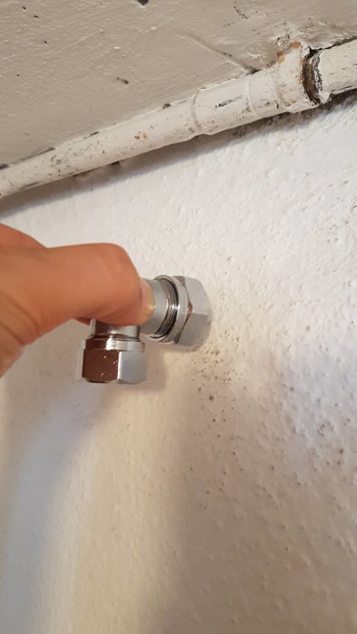 En hand som justerar en vinkelkoppling på ett rör som kommer ut från en vägg.