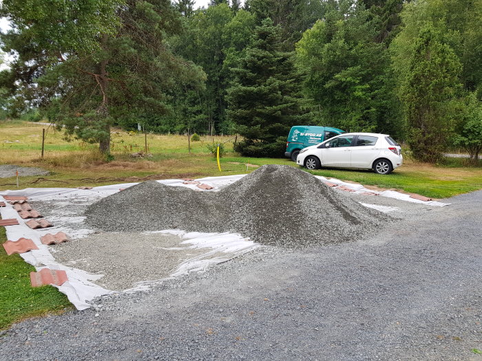 Ny grusad yta för bilparkering med högar av grus 0-18, täckt markduk och parkerad bil i bakgrunden.