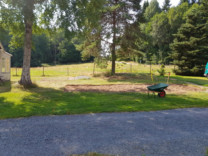 Nyberedd mark för bilparkering med en skottkärra, gräsmatta och träd i bakgrunden.