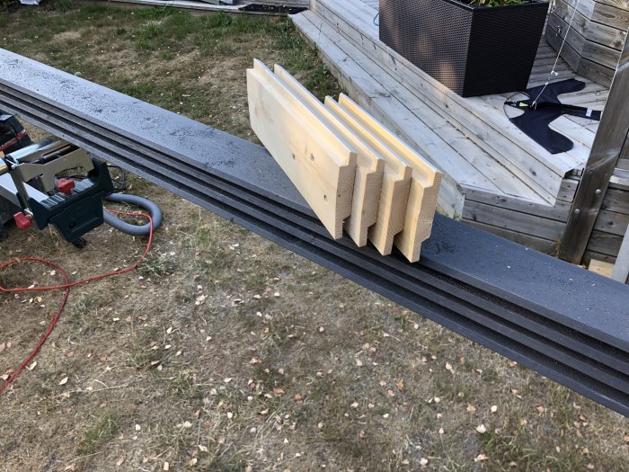 Målade brädor upplagda i en jigg för längdmätning inför panelbyte, med verktyg och plattform i bakgrunden.