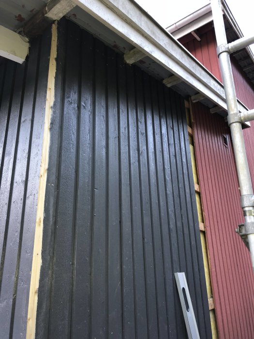 Panelbyte på husgavel med svarta brädor, en vattenpass och mätjigg vid takfoten.