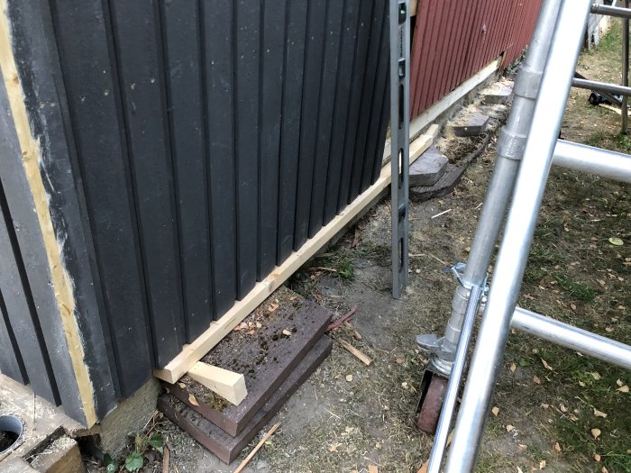 Pågående arbete vid husgavel med påbörjat panelbyte, verktyg och ny panel vid foten av en ställning.