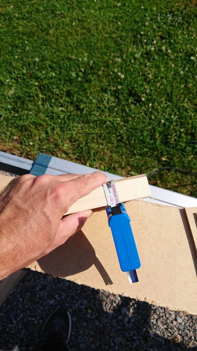 Hand som håller en skjutmått som mäter träbit mot en mall av masonit utomhus.
