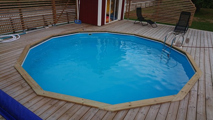 Ovanskuren bild av en blå rund pool inramad av nysågat trä på ett trädäck.
