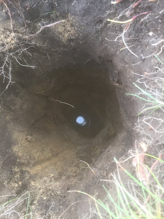 Radontestburk nedsänkt i ett grävt hål i marken under ett bygglovsförberedande radontest.