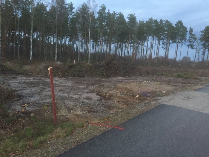 Schaktad tomt med hög vägkant, sandfyllning och rännor för avloppsmatning vid skymning.