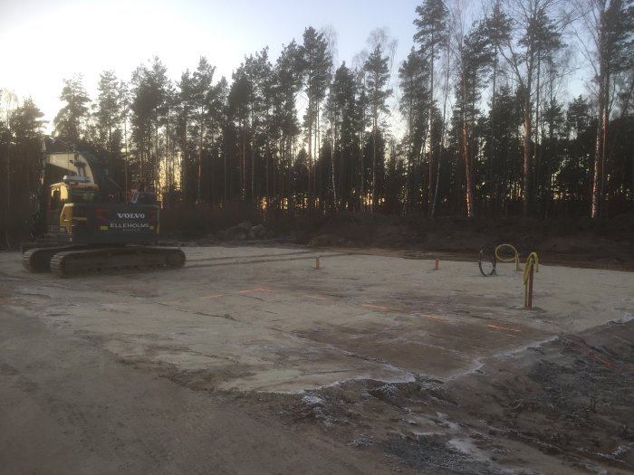 Grävmaskin på en shaktad tomt fylld med sand och rännor för avloppsmatning, vid skymning.