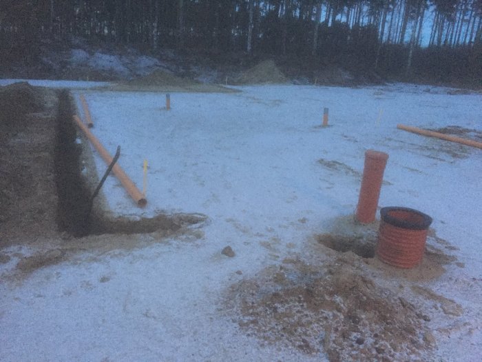 Tomt i skymning med påbörjade grävningsarbeten, sandfyllning och rör för avloppet.