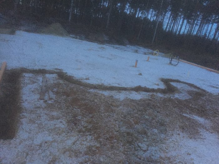 Tomt med utschaktade rännor för avloppsmatning, omgiven av snötäckt mark och skog.